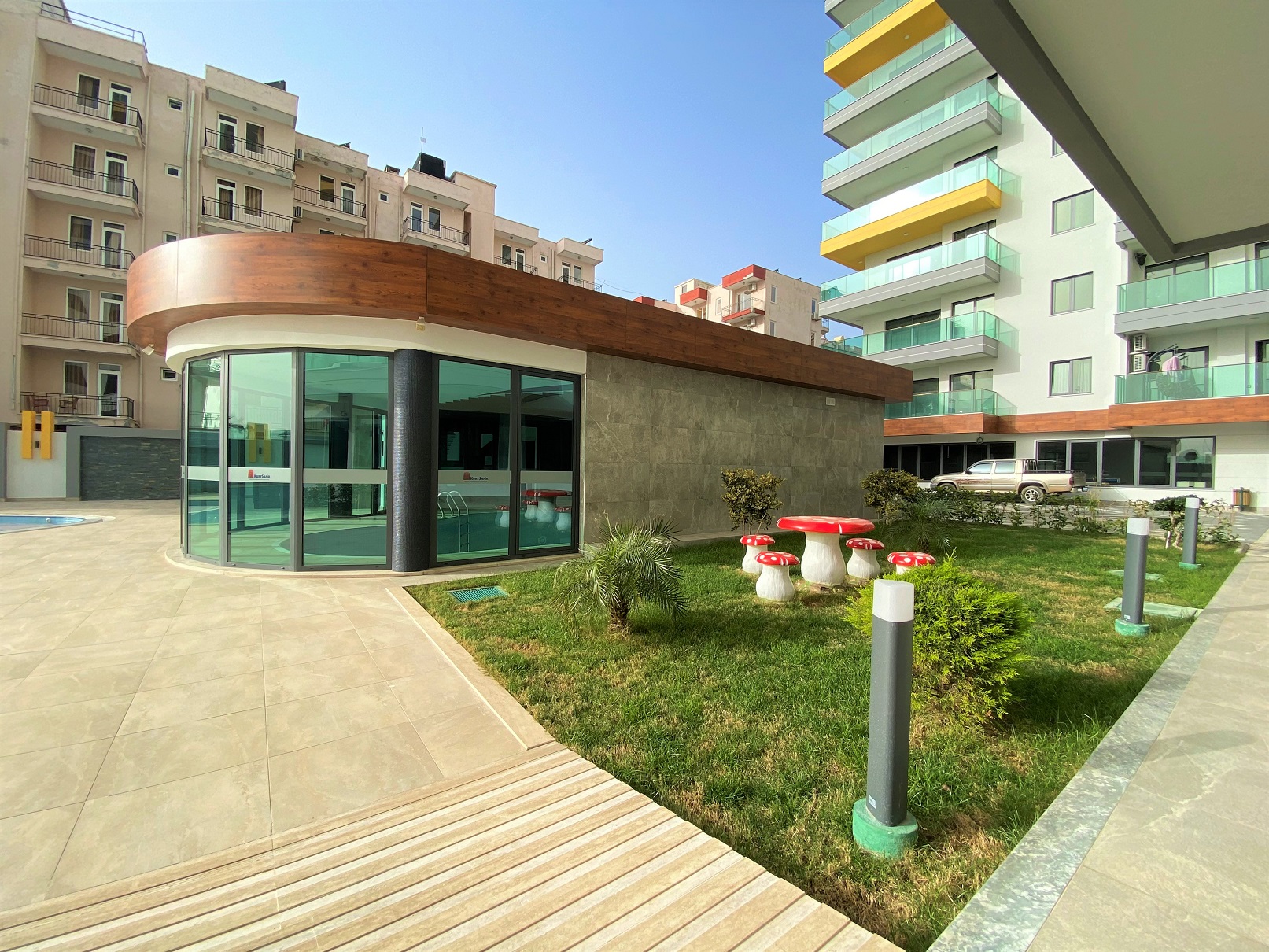 Yeşil panoramik camlı yuvarlak cepheli avlu binası, Mahmutlar’da satışa sunulan kompleksin bahçesinde