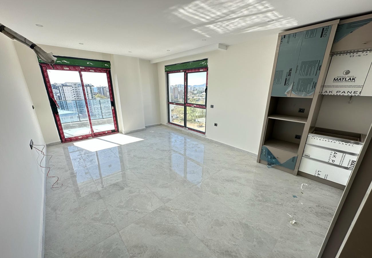 Mutfaklı salonda köşe panoramik camlar, balkon çıkışı ve dağlarla şehir manzarası