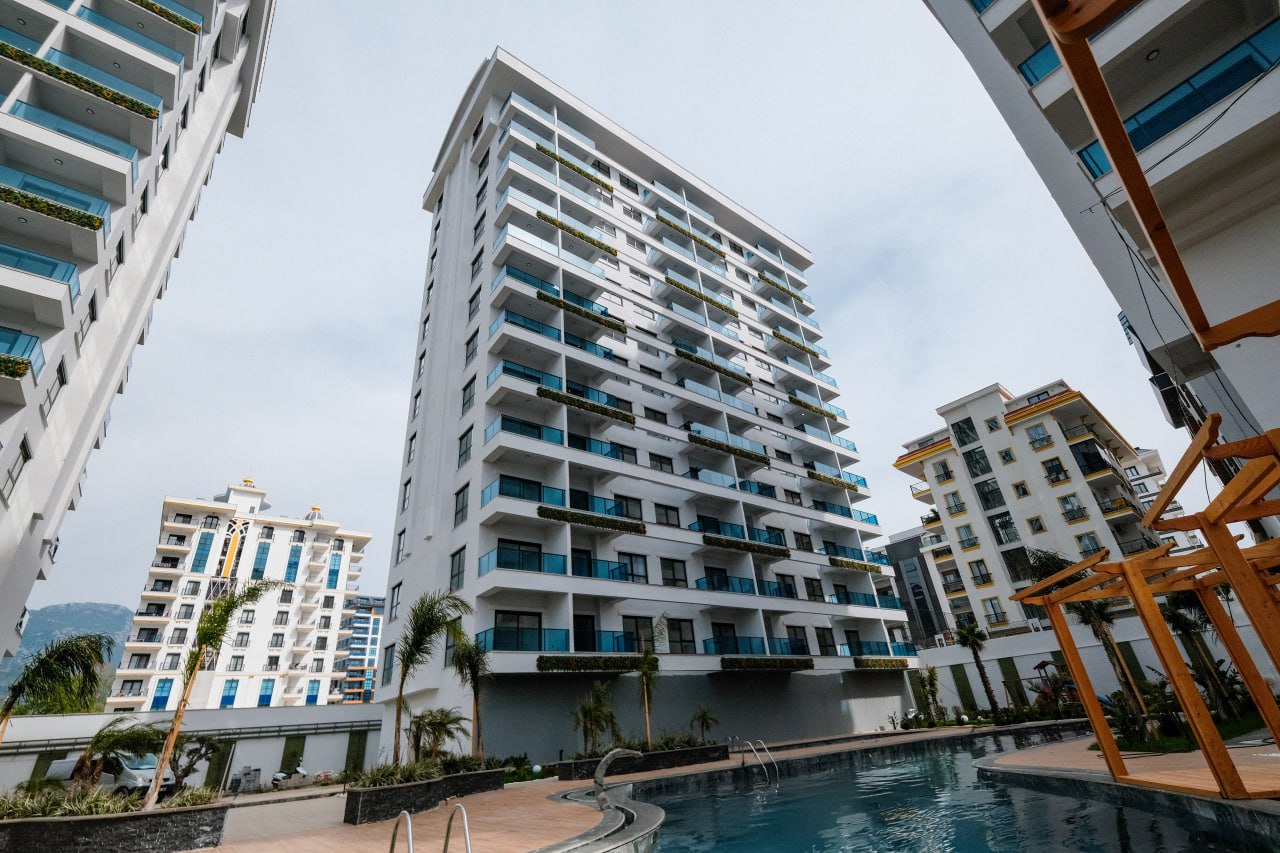 Beyaz yüksek blok önünde açık havuz ve pergola, Türkiye’de satılık 2+1 dairelerin bulunduğu sitede