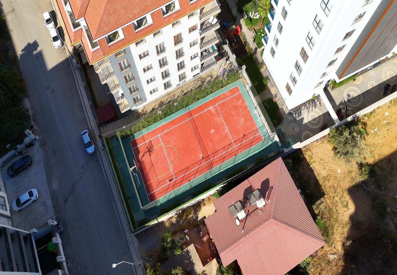 Mahmutlar’da beyaz çizgili kırmızı tenis kortu, satılık konutların yer aldığı blokların yanında