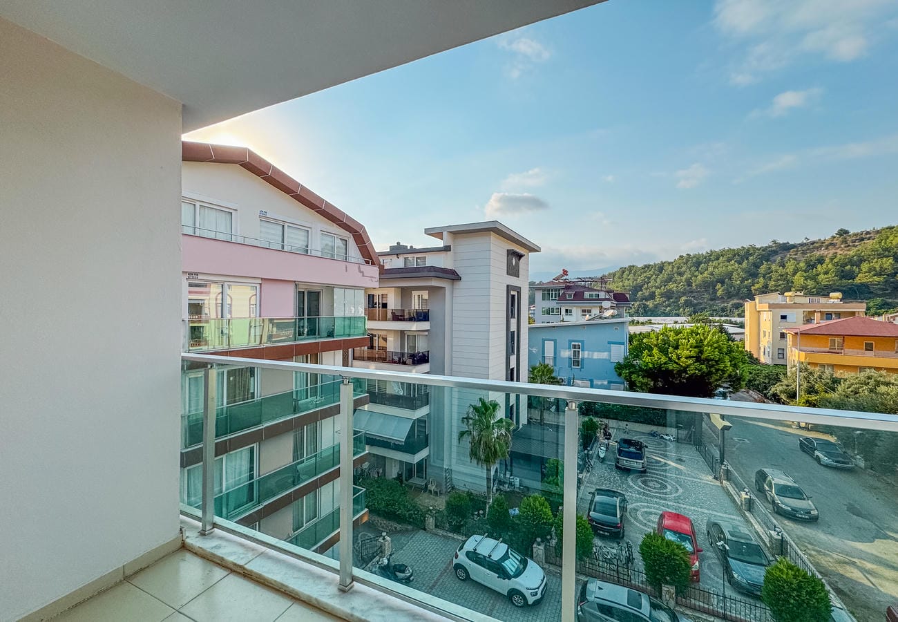 Cam korkuluklu balkon ve park edilmiş araçların görüldüğü yeşil yamaç manzarası, rezidansta