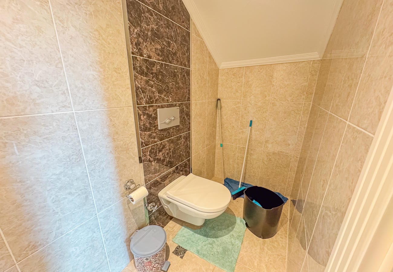 Duvara asılı klozet ve bej seramikli banyo, koyu dekoratif şeritli mekânda