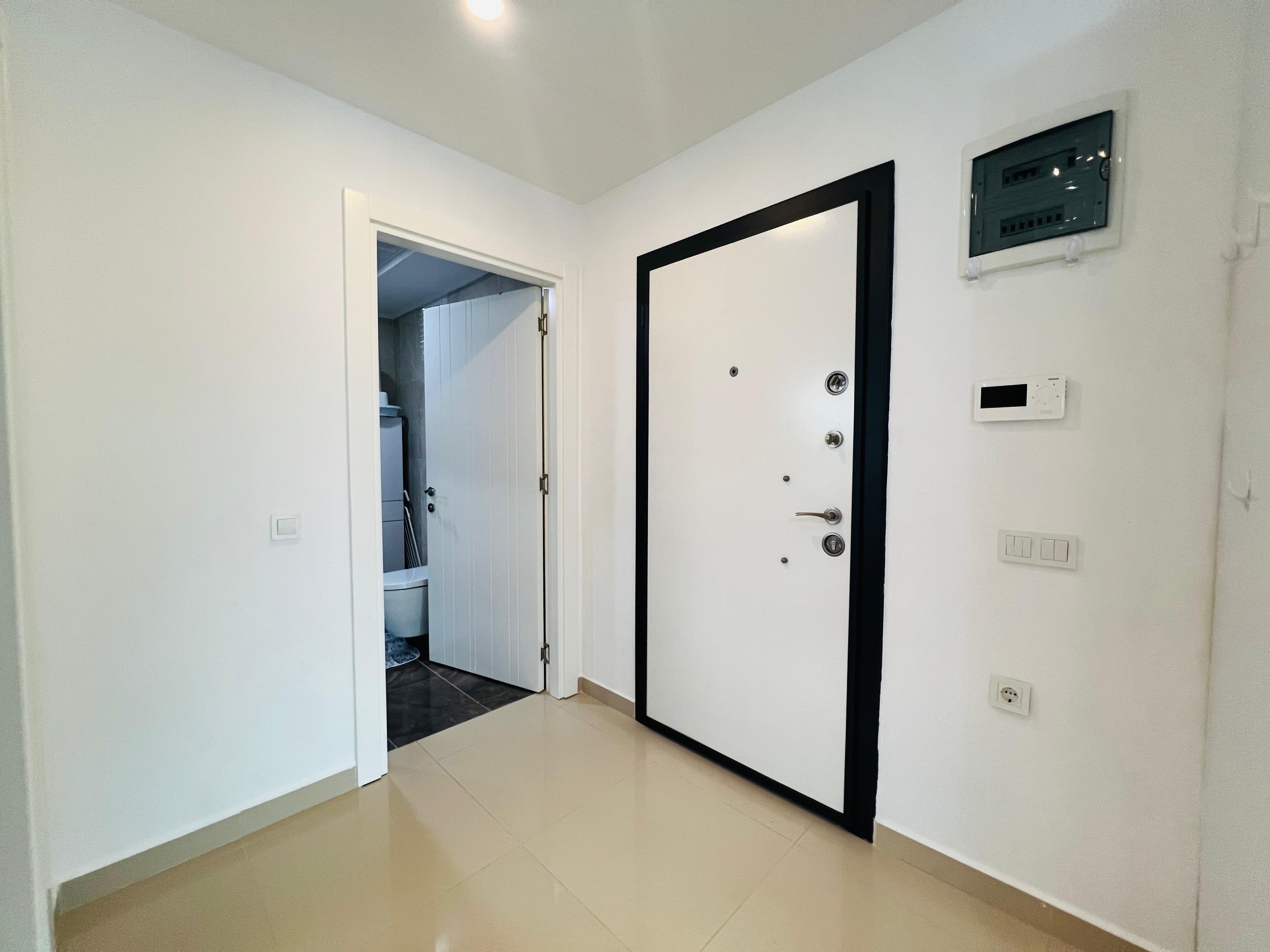 White entrance door with black trim and an open bathroom doorway in a bright tiled hallway
