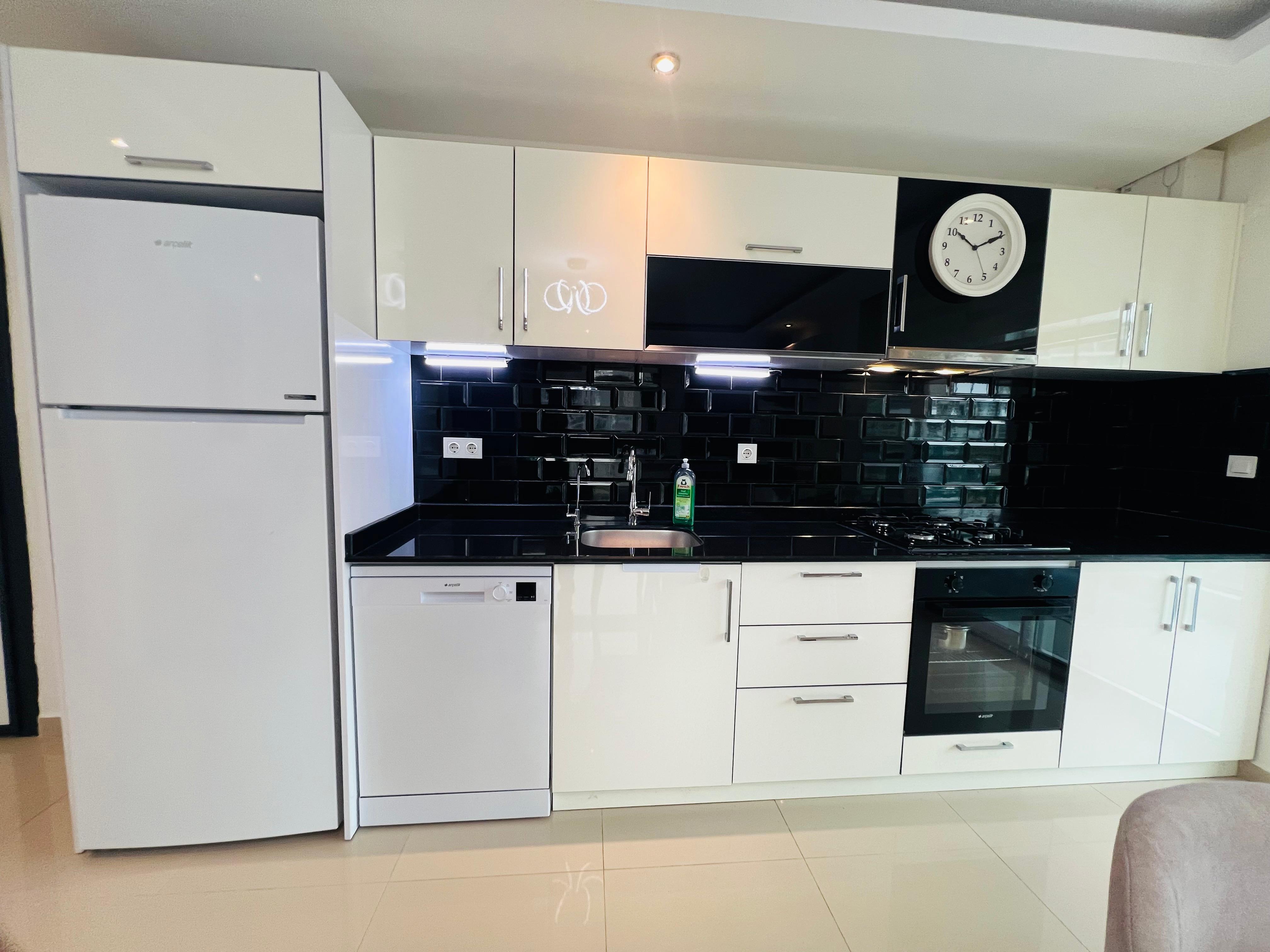 Kitchen with white cabinets black splashback and built-in oven in a flat in Avsallar