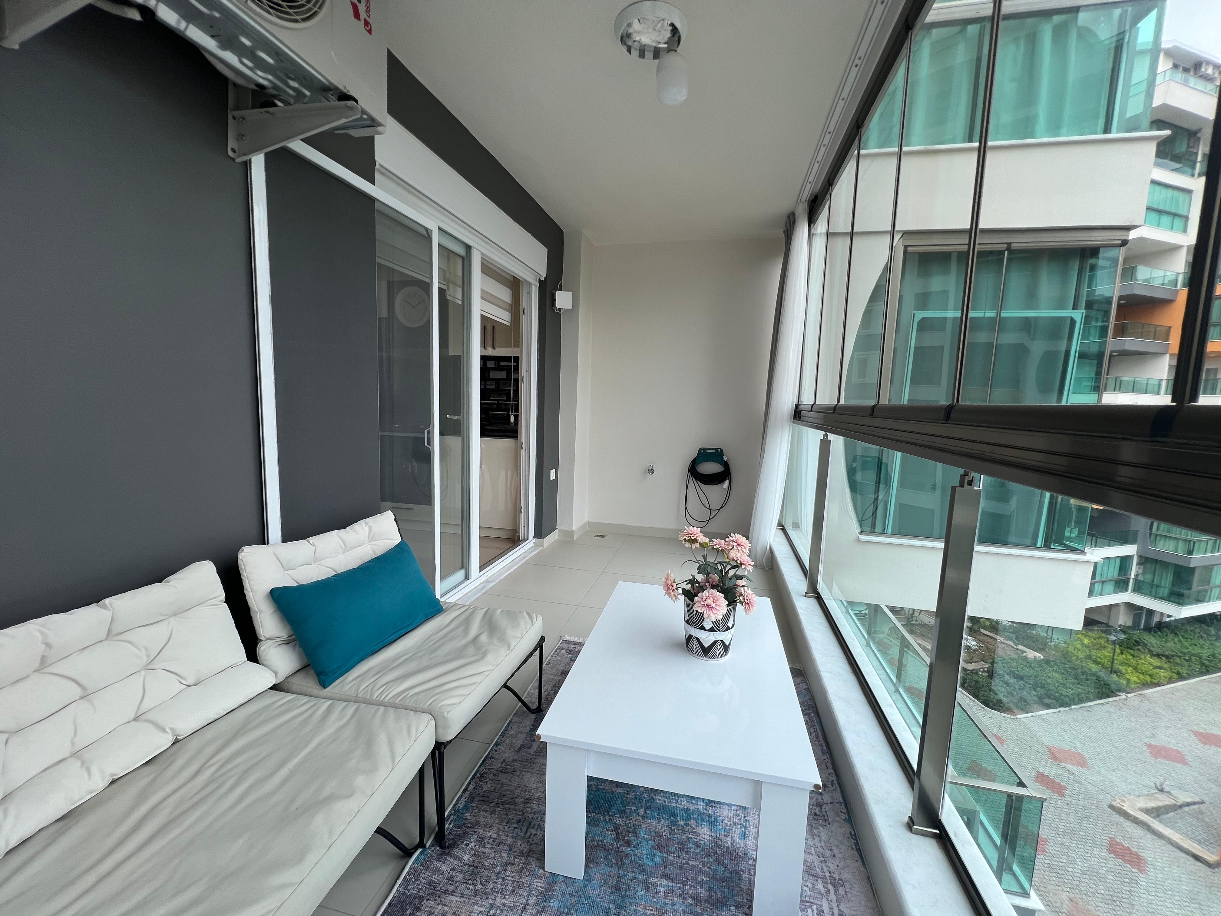 Glazed loggia with a white sofa and views of landscaped grounds at an apartment in Avsallar, Turkey
