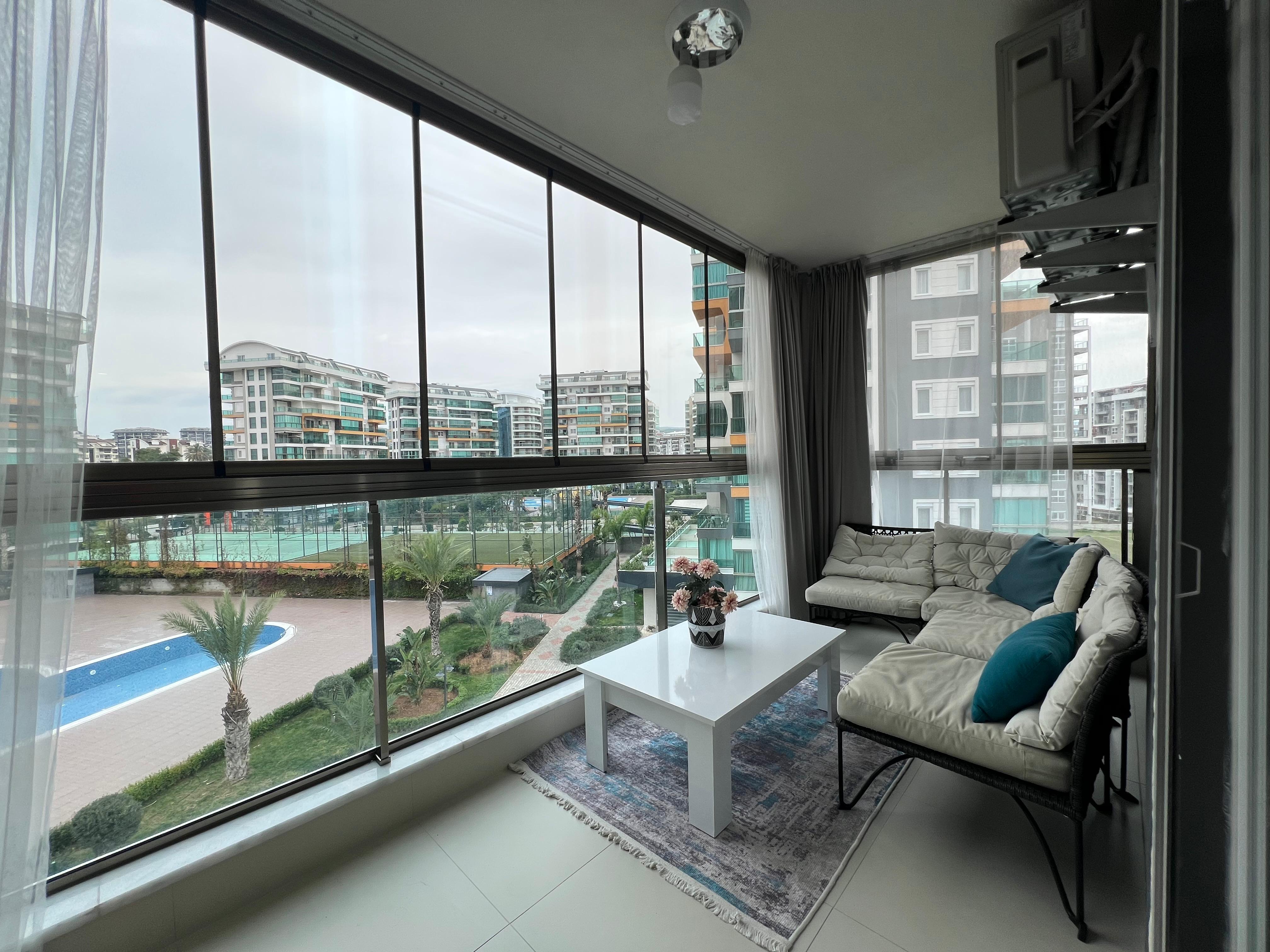 Living room with a light sofa and pool view through panoramic glazing in an apartment for sale