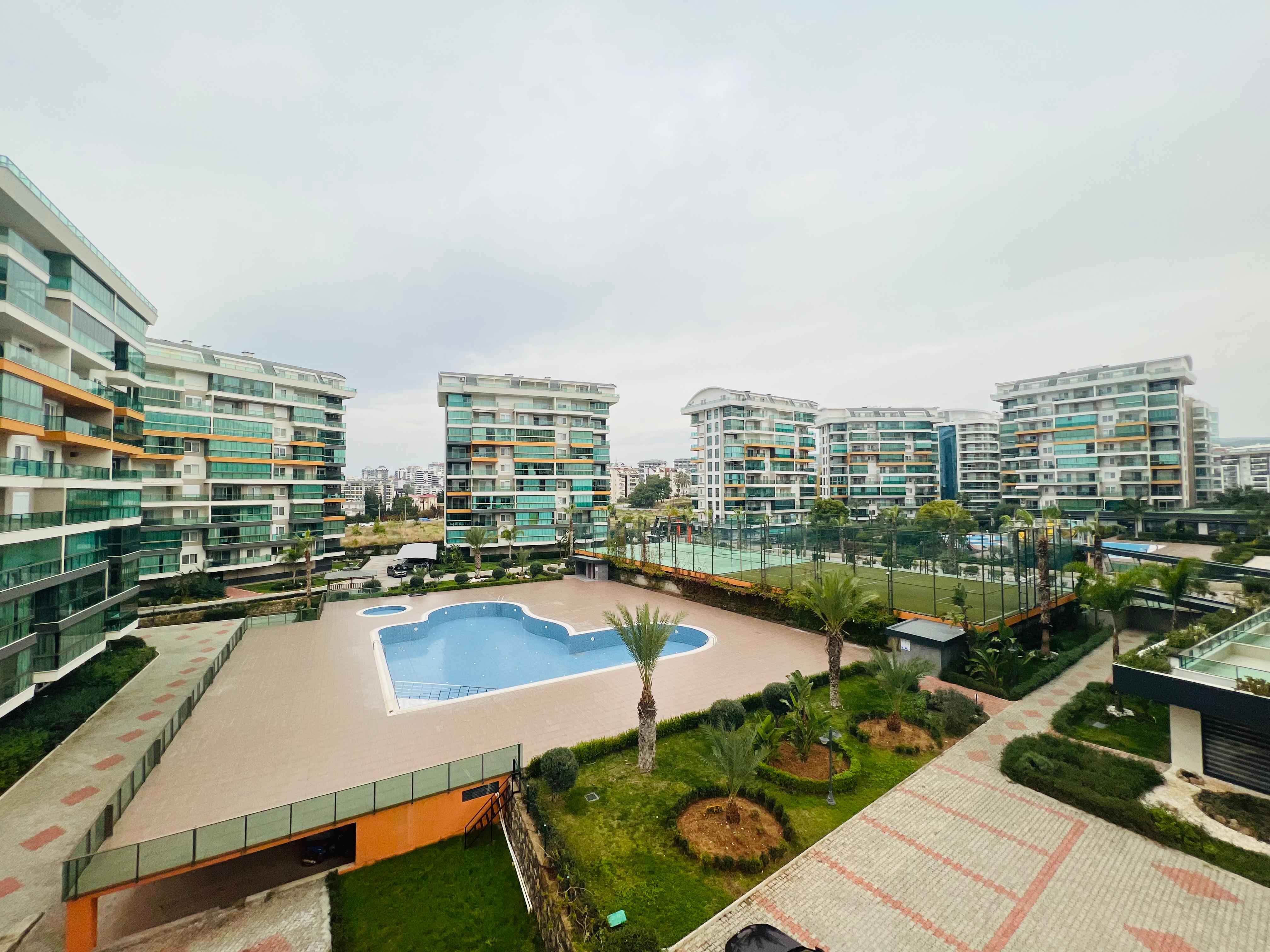 Outdoor pool with palms and multi-storey buildings at a complex where apartments are for sale in Turkey