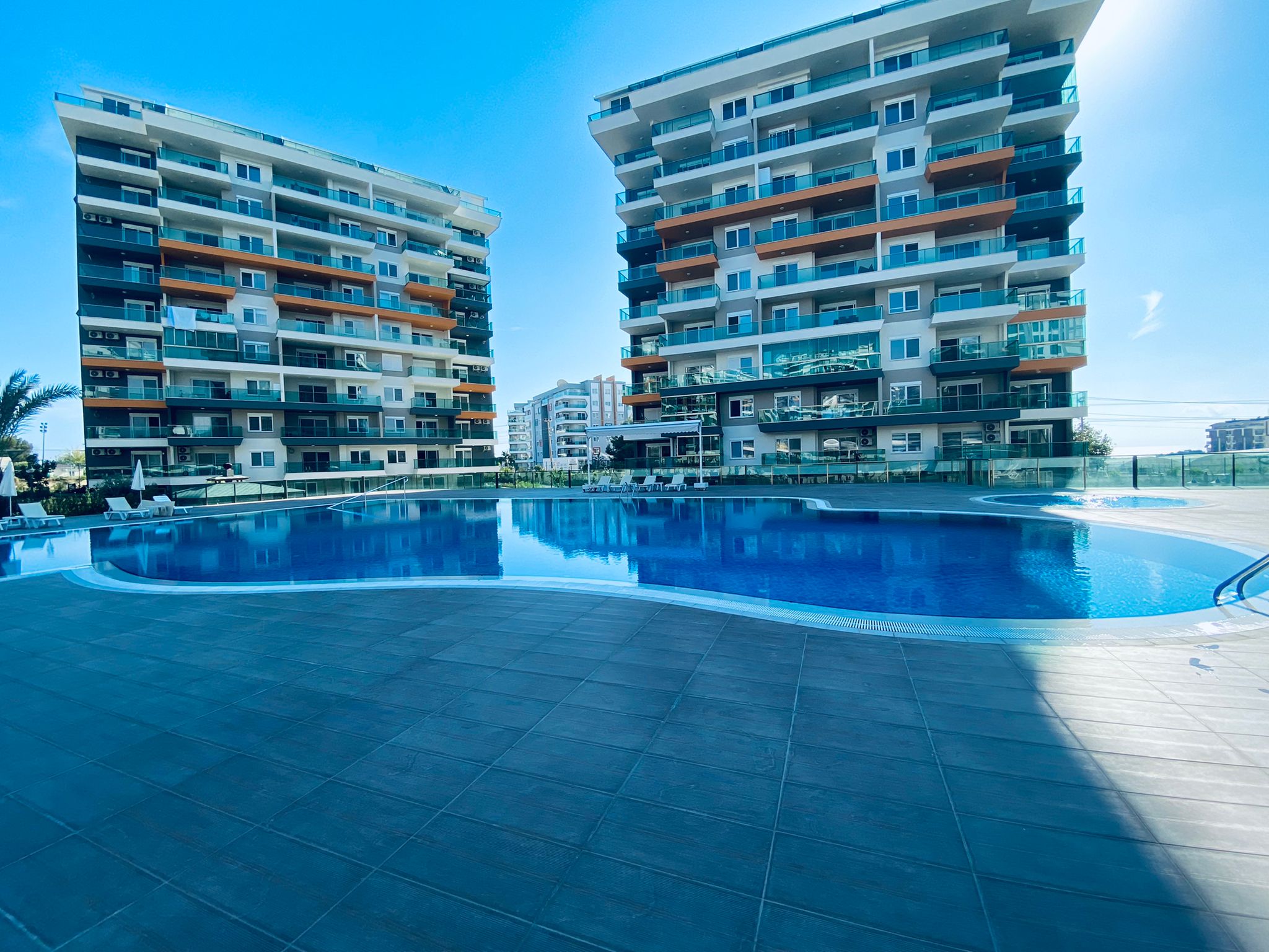 Large outdoor pool with white umbrellas and palms at a complex where apartments are for sale