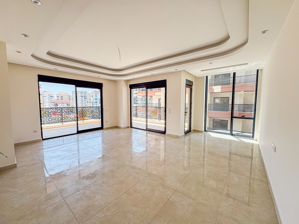 Türkiye’de satılık dairenin geniş salonunda üç panoramik pencere ve balkon çıkışları