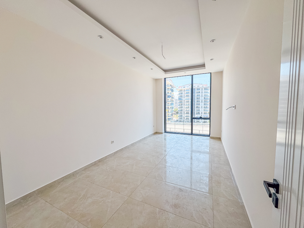 Mahmutlar’daki dairenin dar yatak odasında balkon kapısı, spot ışıklar ve şehirdeki binalar