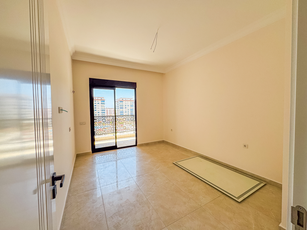 Açık renk duvarlı yatak odasında balkon kapısı, ajurlu korkuluk ve zeminde dekoratif panel