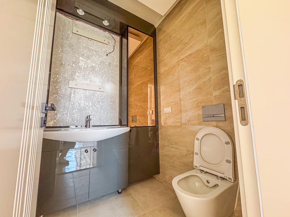 Denize yakın banyoda beyaz asma klozet, gri lavabo dolabı ve siyah çerçeveli ayna