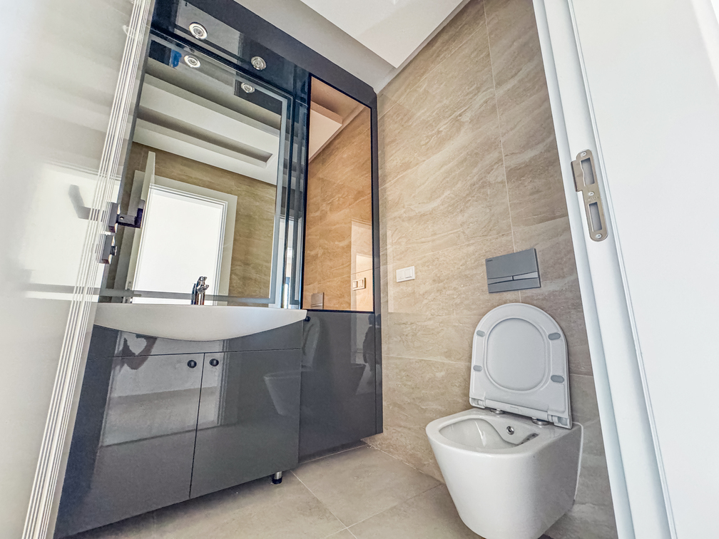 Koyu gri lavabo dolabı, siyah çerçeveli ayna ve lavabo üstünde açık beyaz raflı banyo