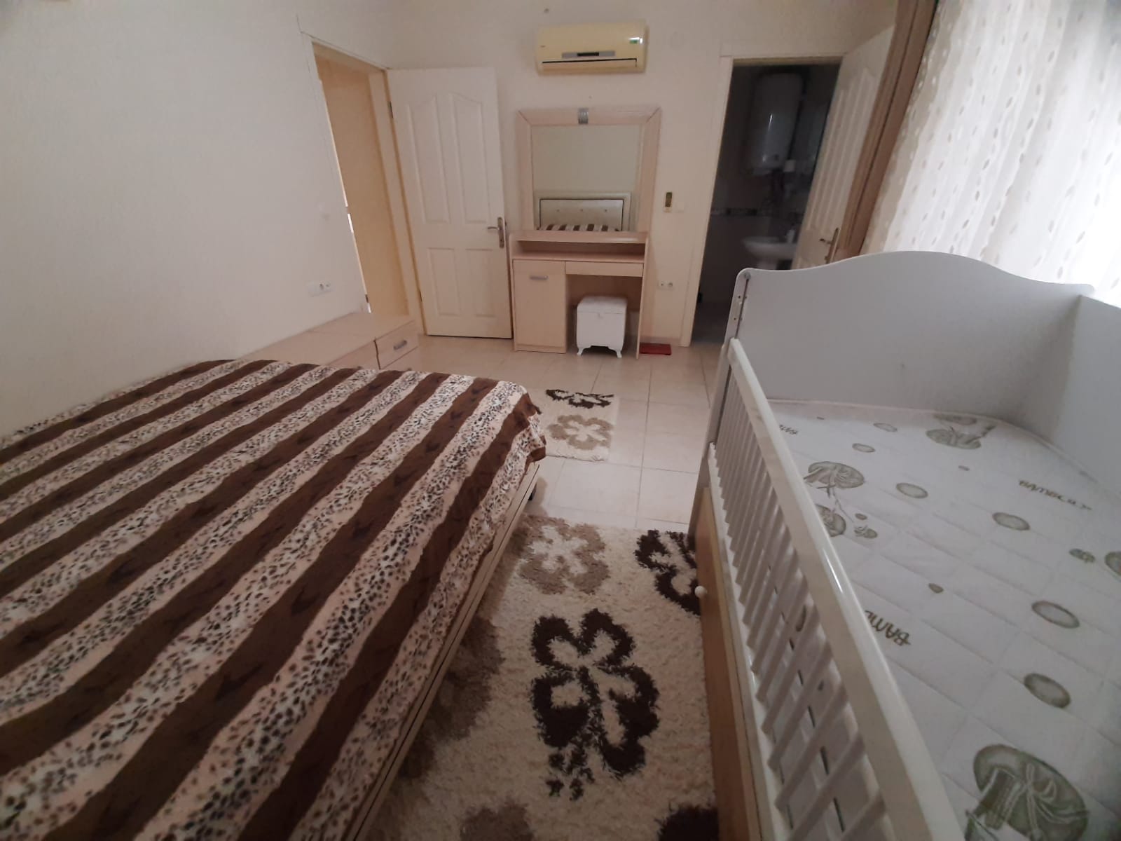 Mahmutlar’daki dairenin yatak odasında çift kişilik yatak, tuvalet masası ve banyo kapısı