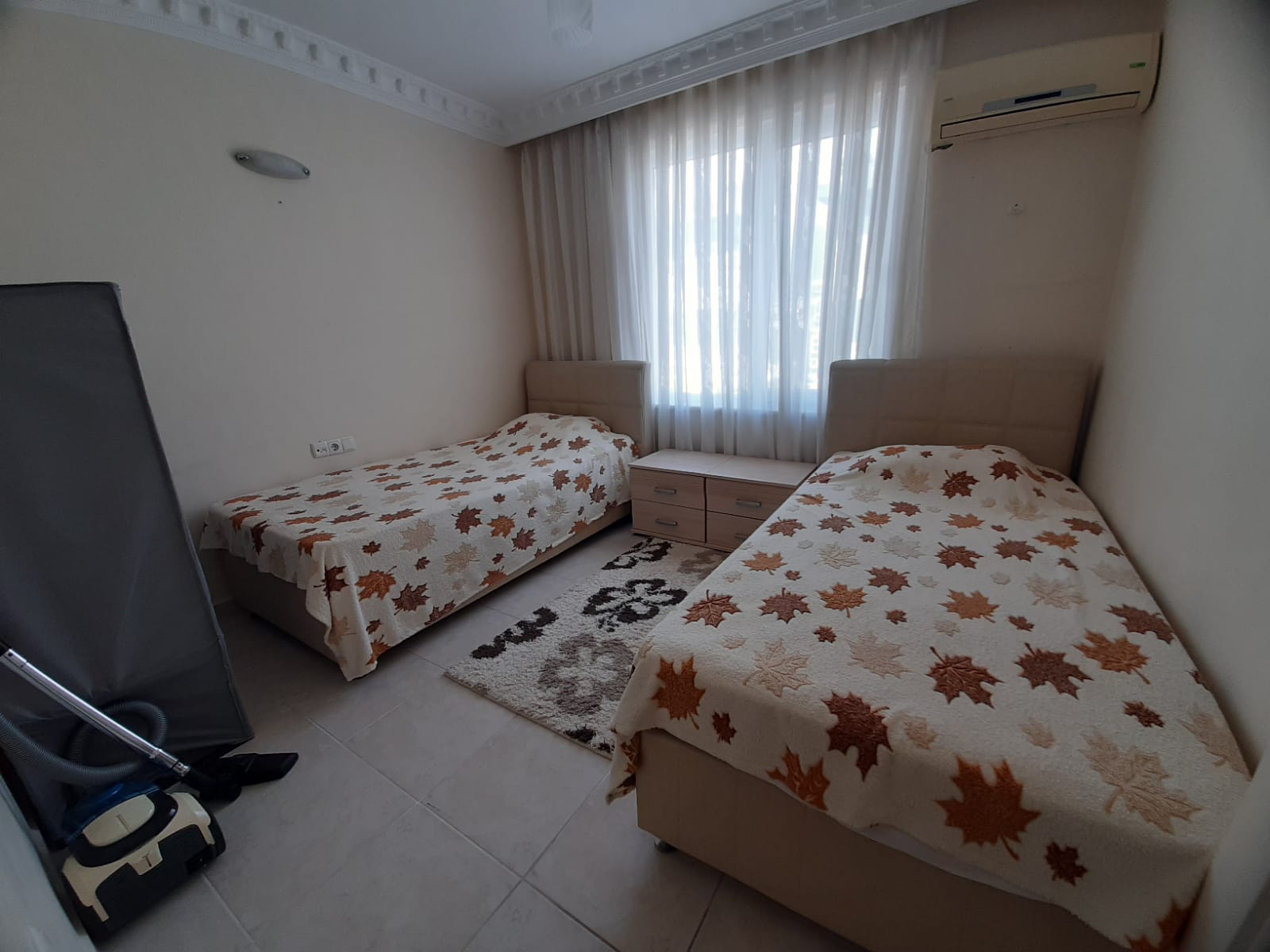 Yatak odasında sonbahar yaprak desenli iki tek kişilik yatak ve katlanmış ütü masası