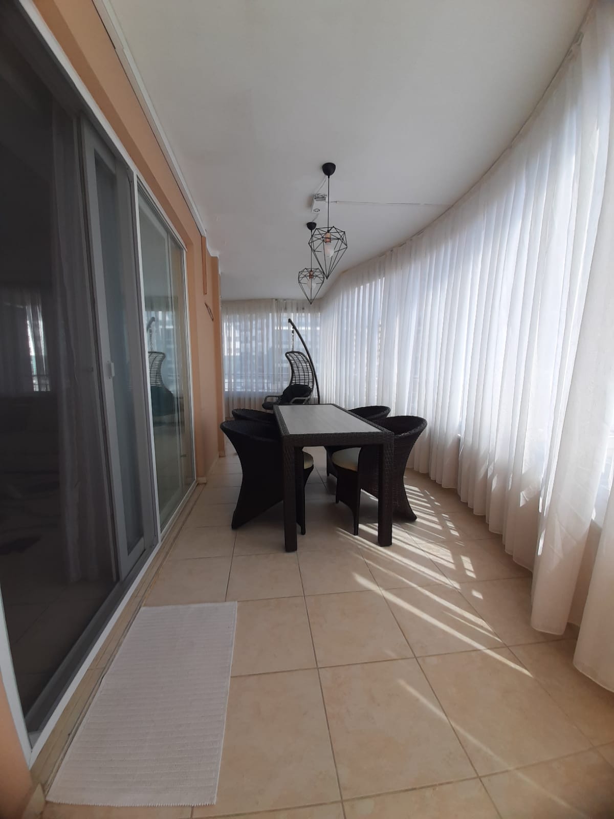 Mahmutlar’da uzun balkonda koyu ahşap yemek masası, dört sandalye ve asılı örgü koltuk