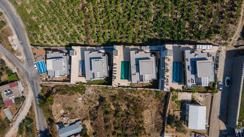 Вид сверху на четыре виллы с прямоугольными бассейнами и мощёными террасами в Каргыджаке, Турция