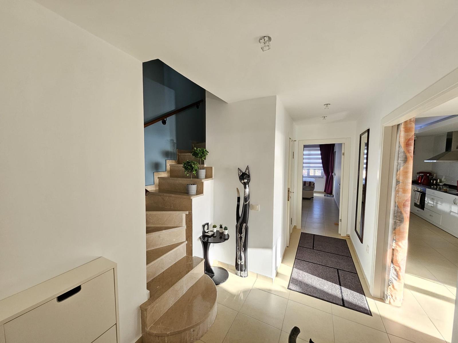 Beyaz şifonyerli penthouse holünde bej basamaklı spiral merdiven ve koridor halısı