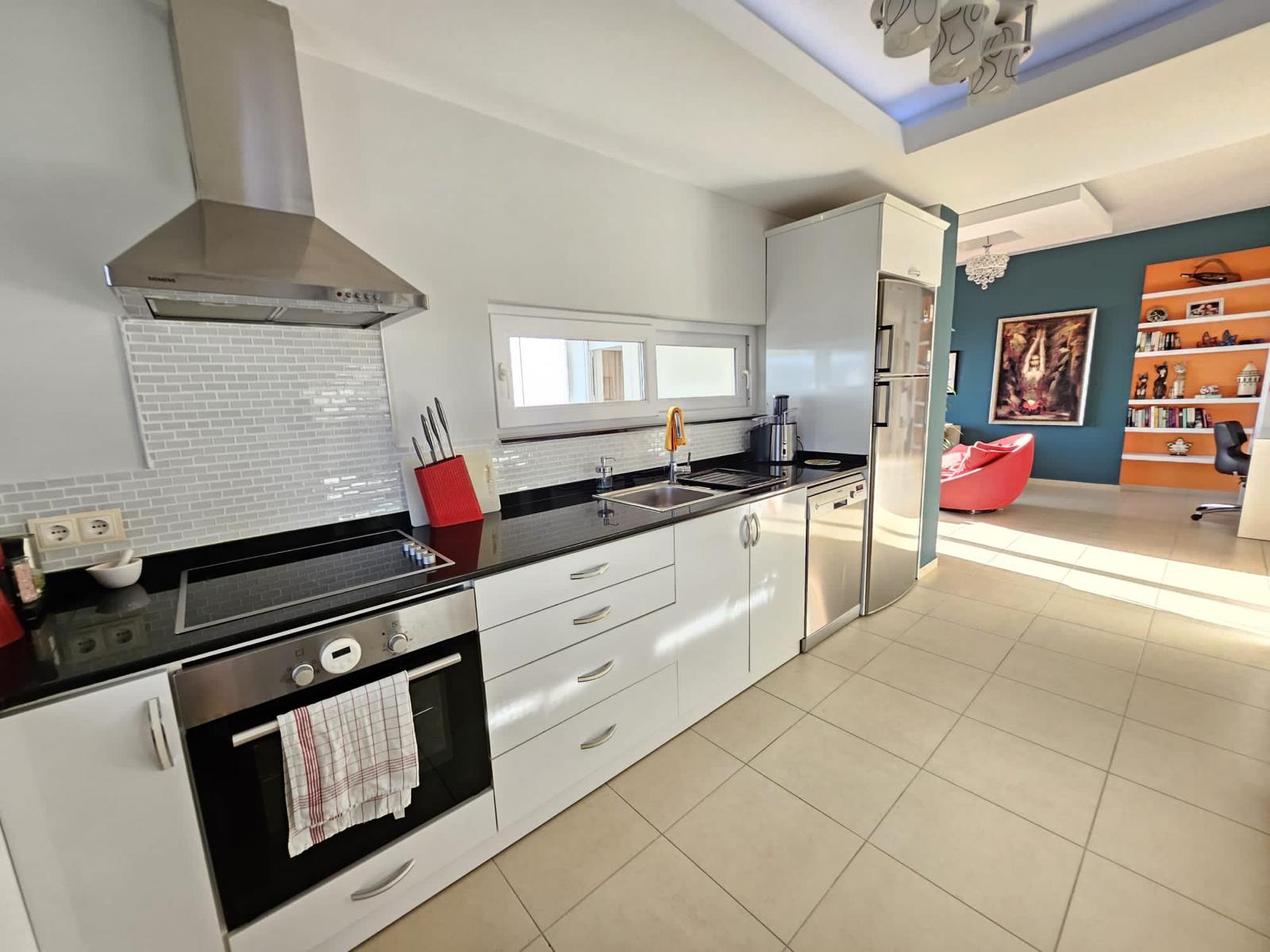 Mahmutlar’daki penthouse mutfağında siyah tezgâh, pencere altı evye ve salona geçiş