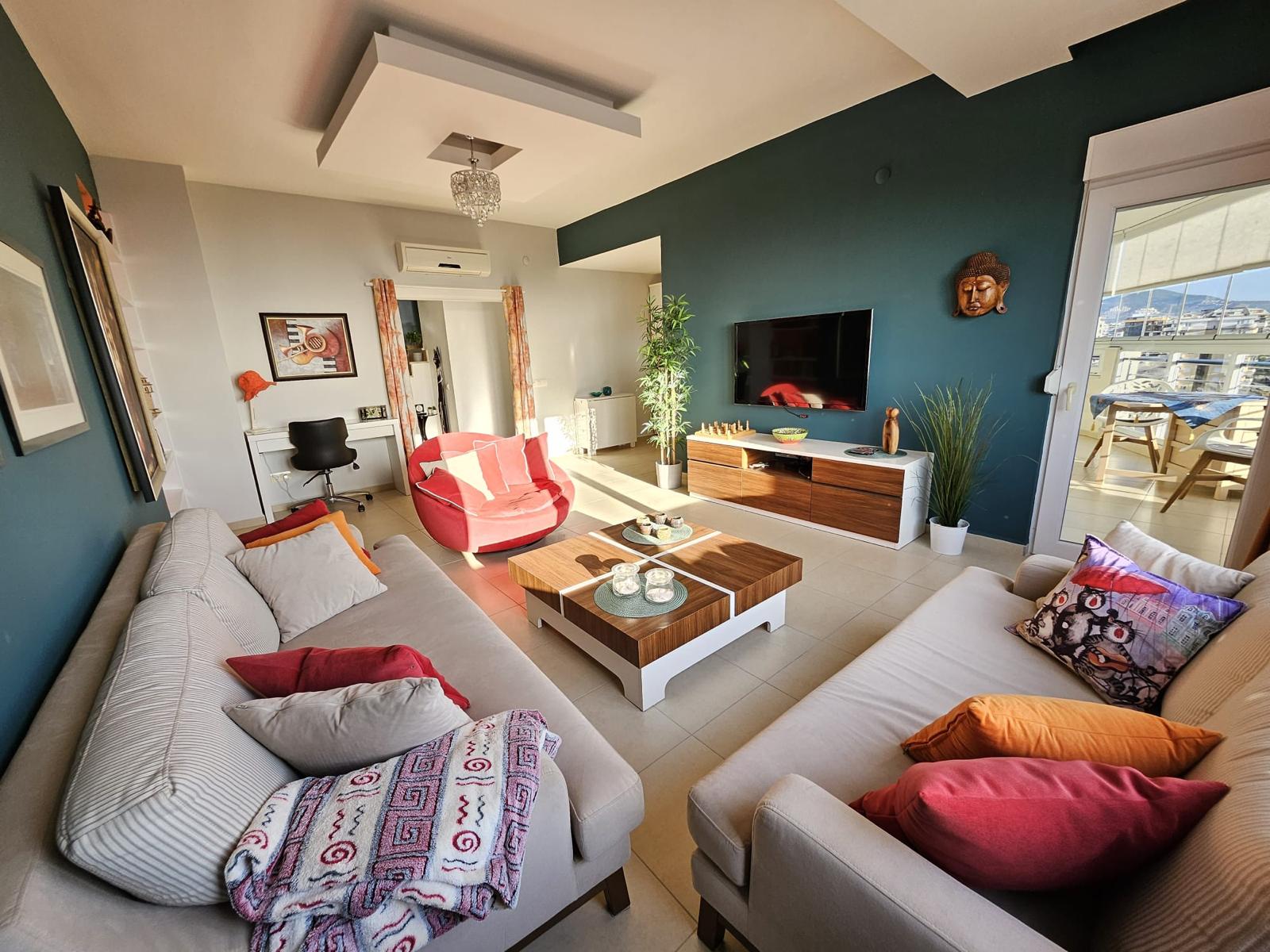 Açık renkli iki kanepeli penthouse salonunda kırmızı koltuk ve terasa açılan panoramik kapı Türkiye’de satılık