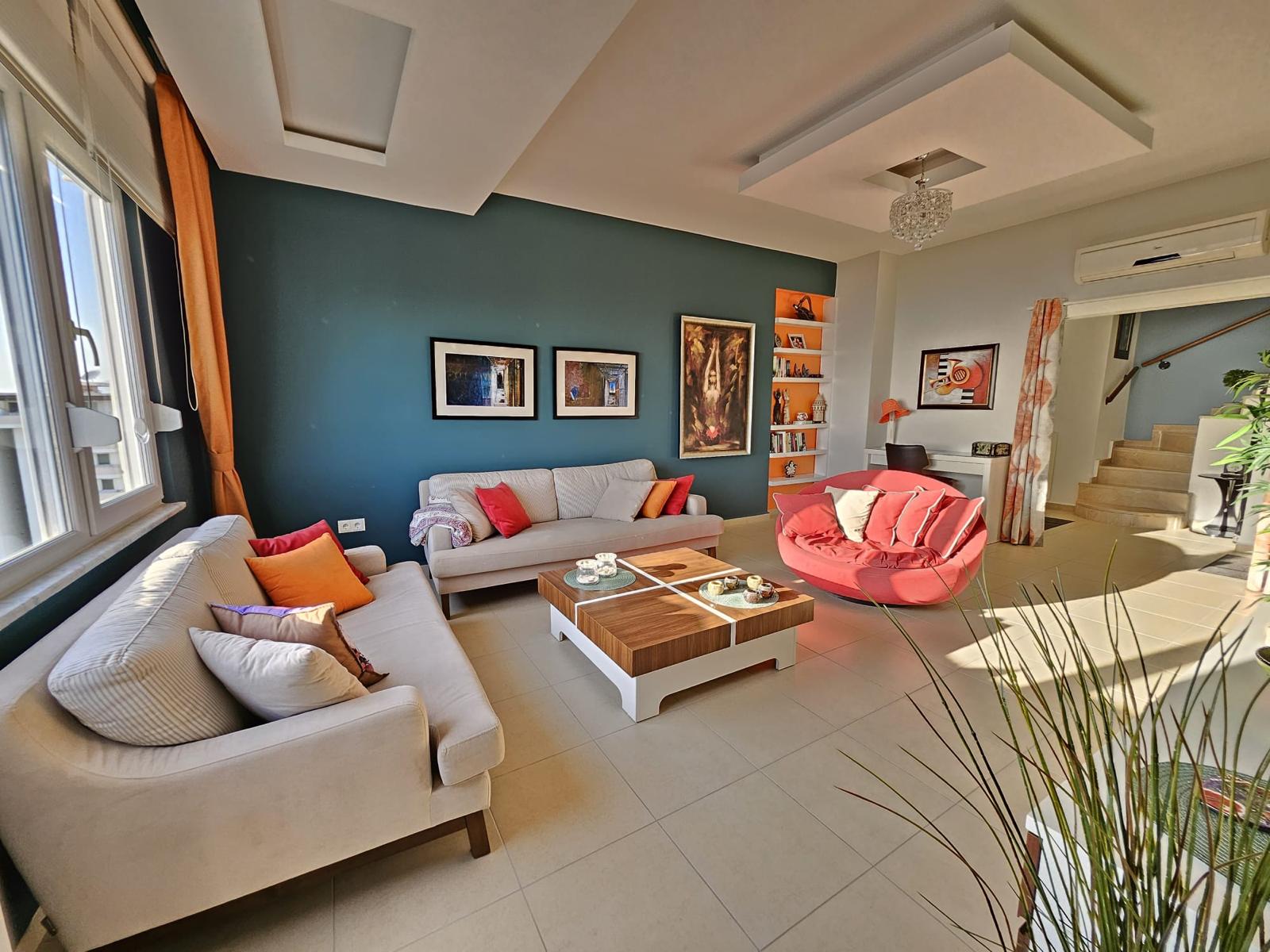 Penthouse salonunda köşe kanepe, kırmızı koltuk ve kitaplı turuncu gömme raflar