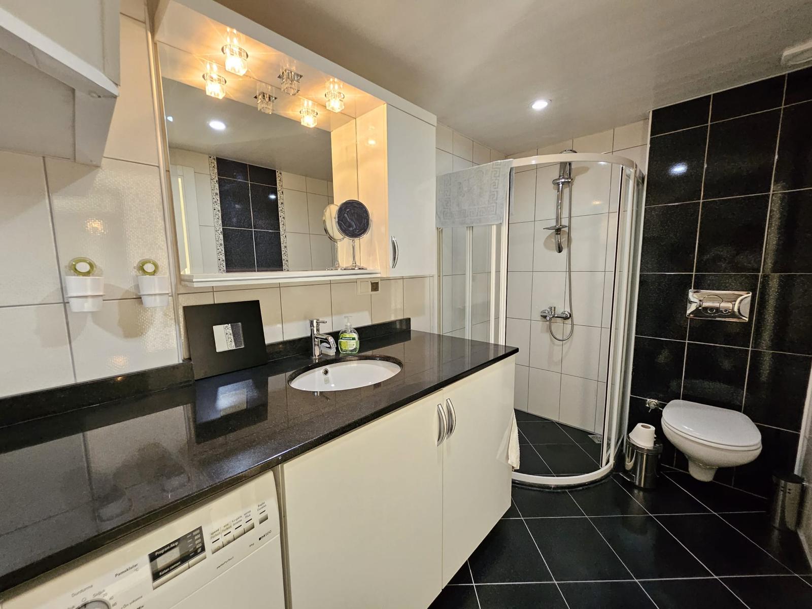 Penthouse banyosunda köşe duş kabini, siyah beyaz seramikler ve çamaşır makinesi