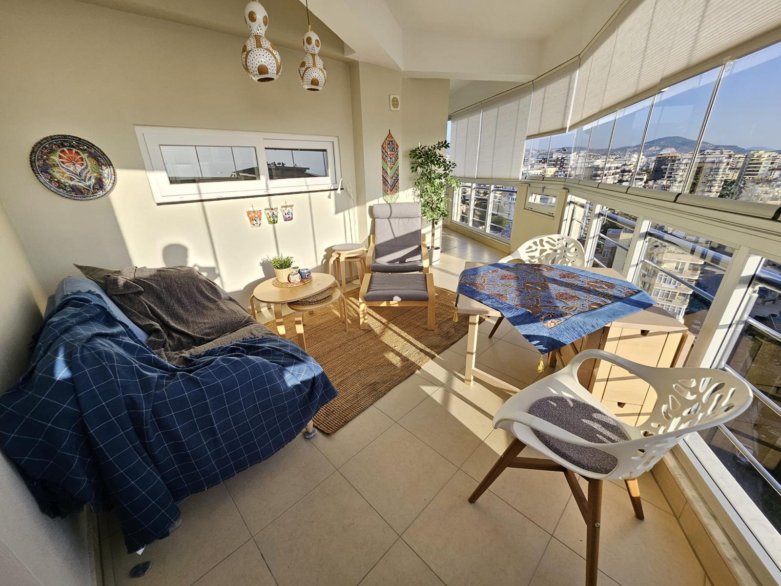 Satılık dairenin salonunda panoramik camlar, ikili kanepe ve örtülü yemek masası