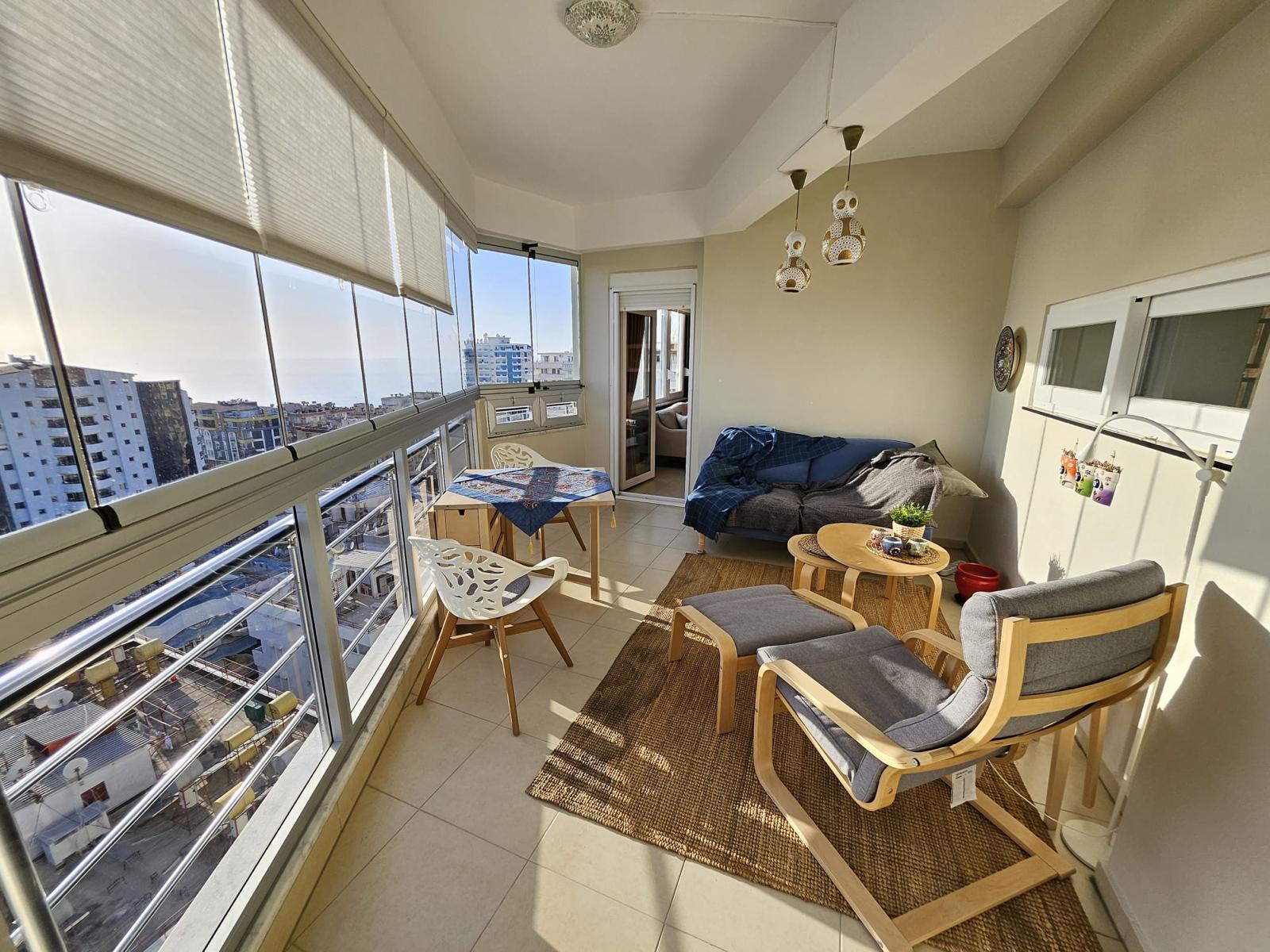 Mahmutlar’daki penthouse salonunda köşe panoramik camlar, kanepe ve şehir yapıları manzarası Türkiye’de
