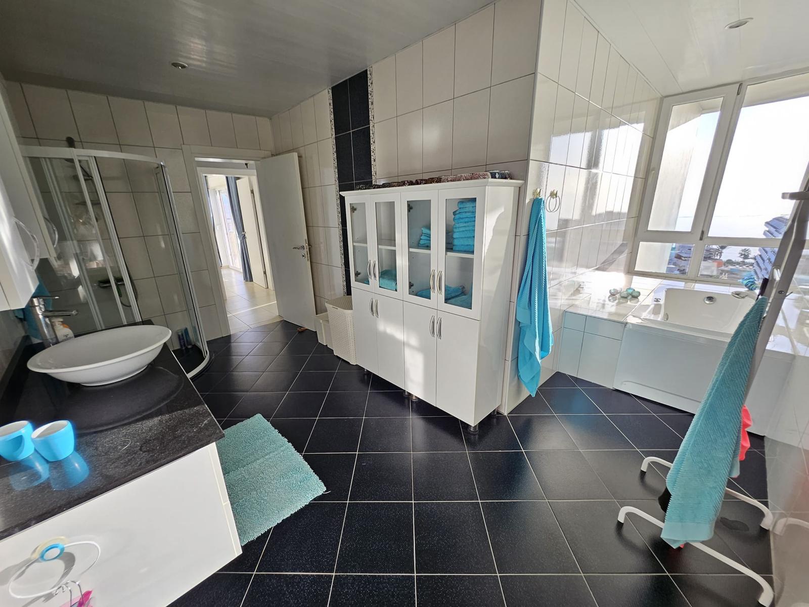 Penthouse banyosunda hidromasajlı küvet, köşe duş kabini ve turkuaz havlular