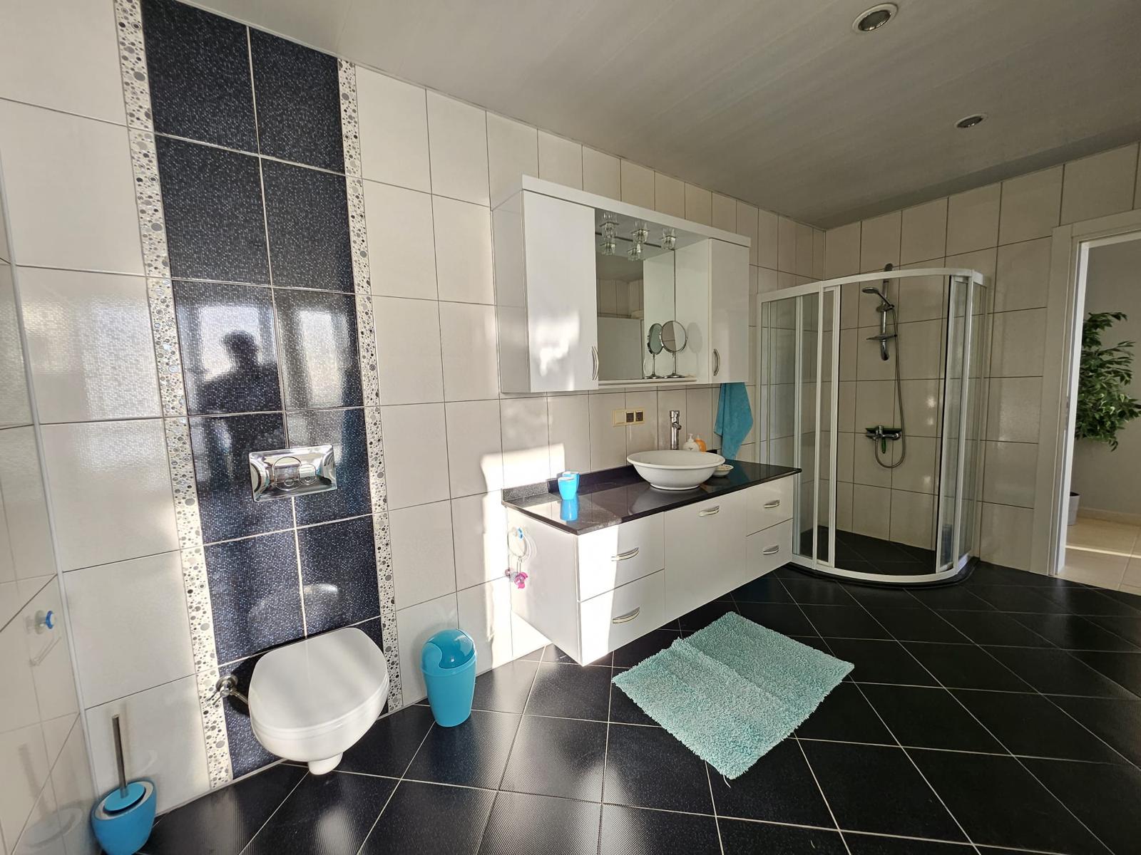 Mahmutlar’daki banyoda köşe duş kabini, çanak lavabo ve duvara asılı klozet
