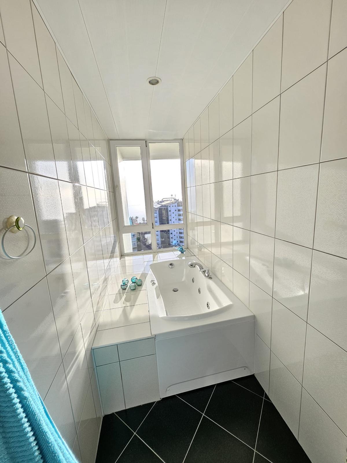 Penthouse banyosunda pencere önündeki hidromasajlı küvet ve şehir yapıları manzarası