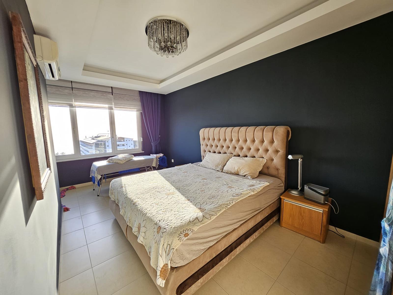 Mahmutlar’daki penthouse yatak odasında bej kapitone başlık, siyah duvar ve kristal avize