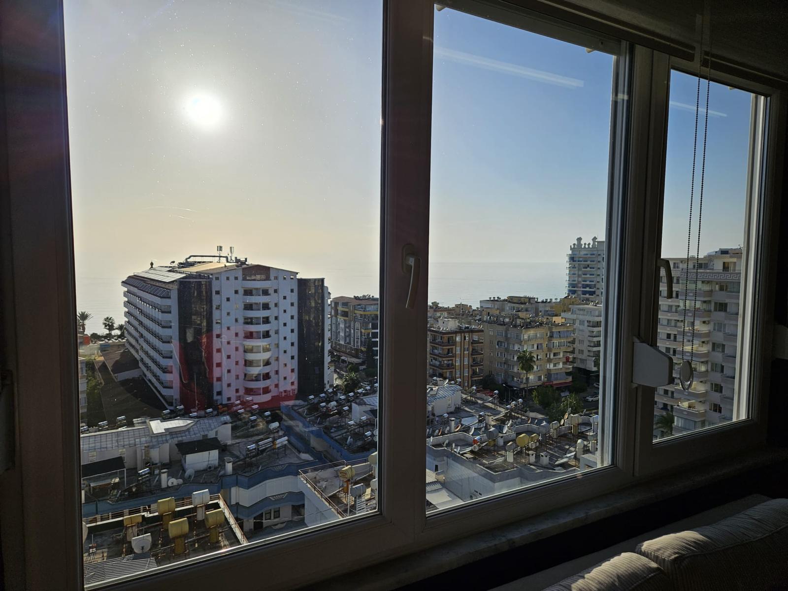 Mahmutlar’daki penthouse panoramik penceresinden şehir yapıları, çatı ve avlu havuzları görünümü