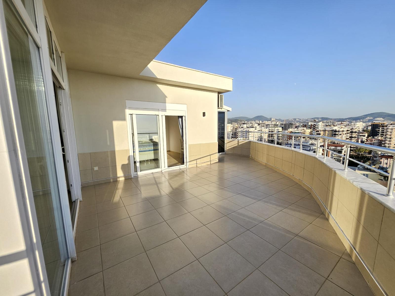 Mahmutlar’da satılık penthouse yanında geniş açık teras, sürgülü cam kapılar ve ufuktaki dağlar