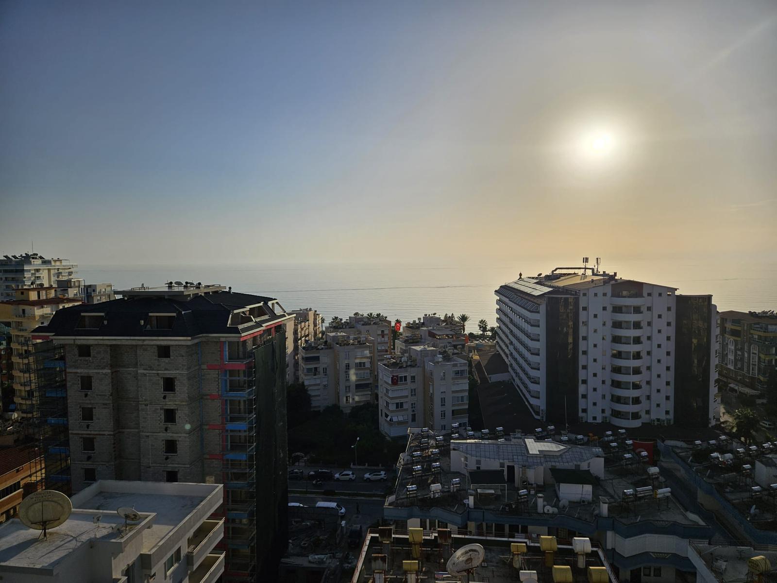 Satılık penthouse içinden deniz, şehir yapıları ve park edilmiş araçların bulunduğu cadde görünümü