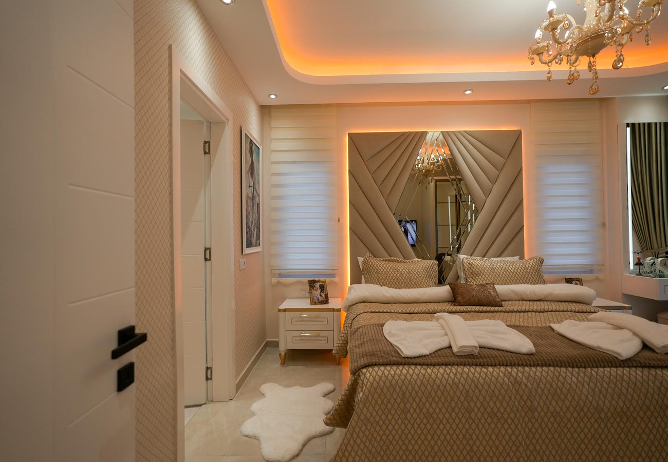 Penthouse yatak odasında bej örtülü çift kişilik yatak ve aynalı başlık