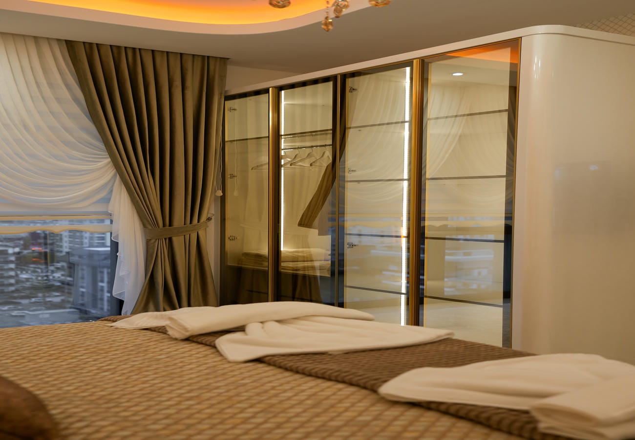 Penthouse yatak odasında kahverengi örtülü çift kişilik yatak ve akşam şehir manzarası