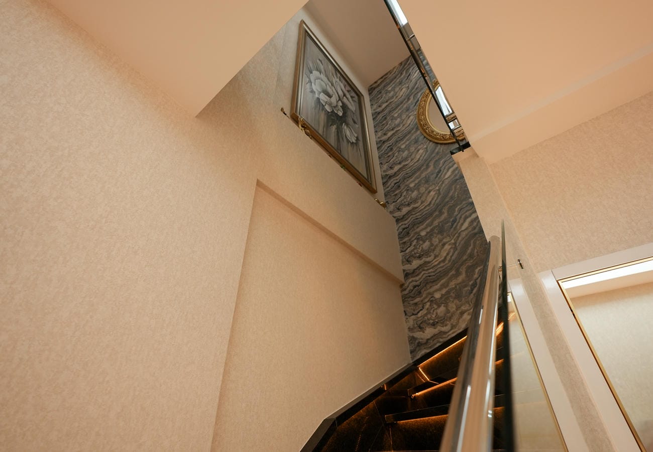 Alanya'daki penthouse merdiveninde dalgalı taş desenli duvar, siyah basamaklar ve şerit aydınlatma