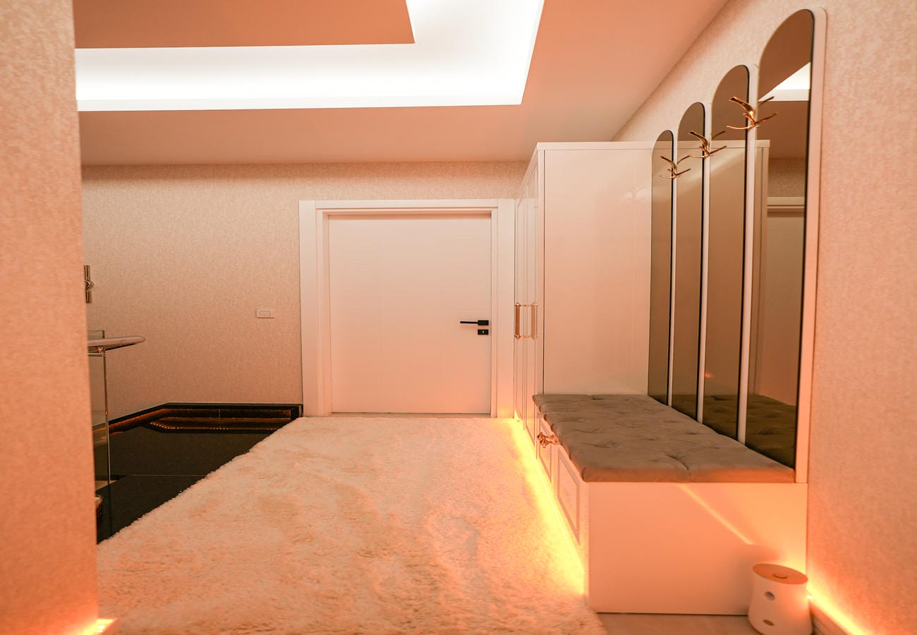 Penthouse antrede gri kapitoneli bank, yüksek kemerli aynalar ve altın renk duvar askıları