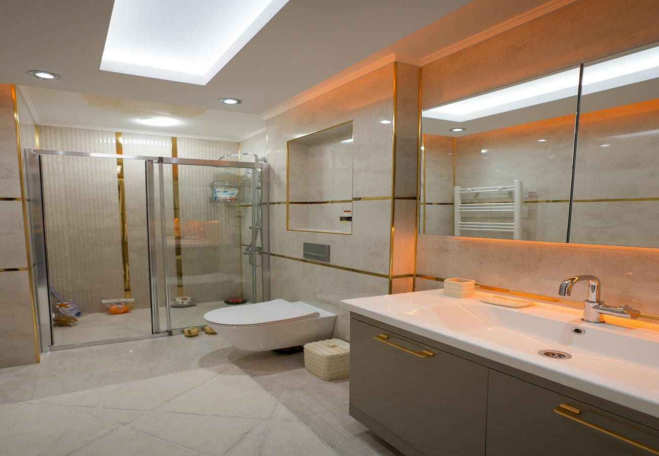 Penthouse banyosunda bağımsız beyaz küvet, cam duşakabin ve çift lavabolu geniş dolap