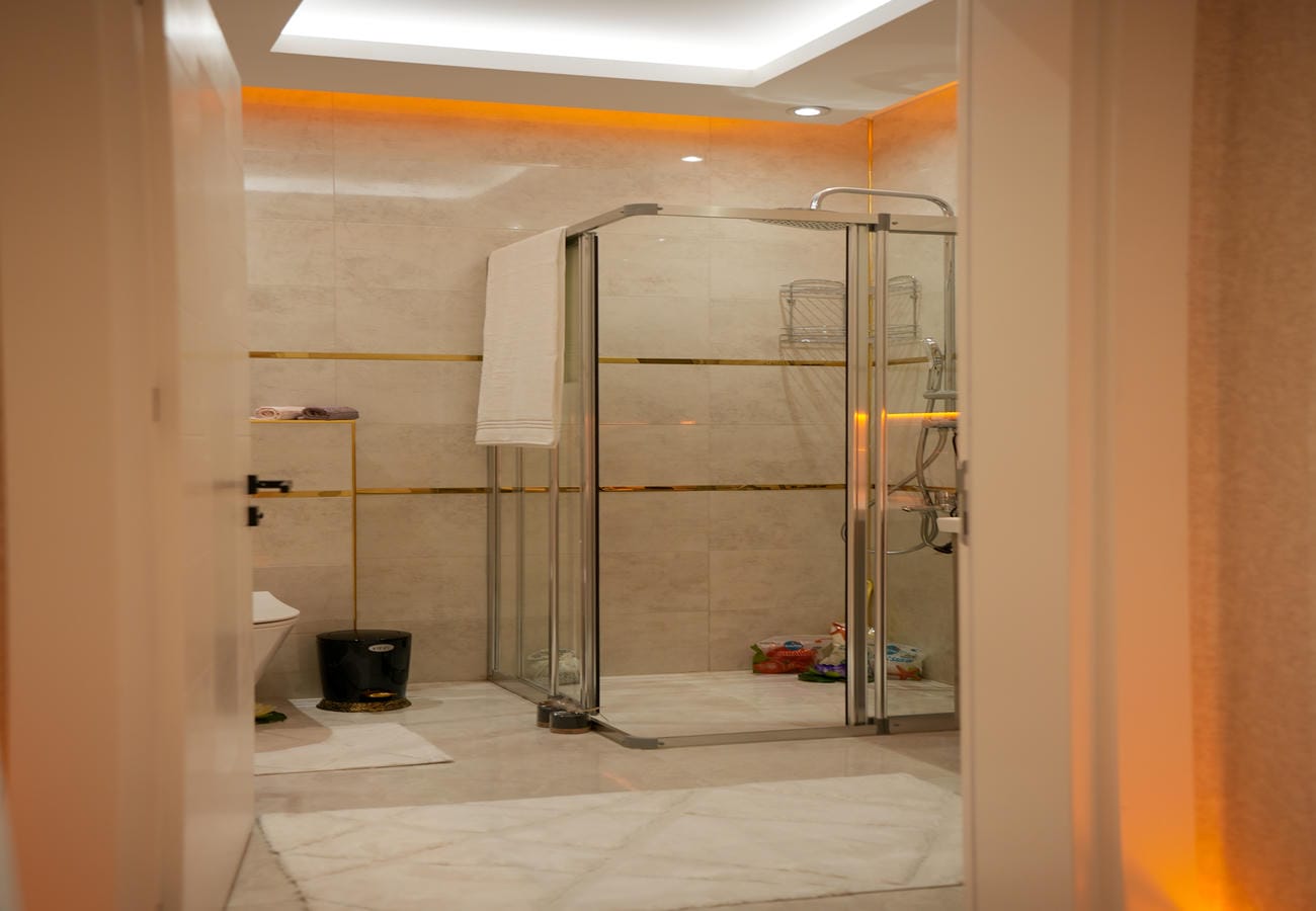 Alanya'daki penthouse banyosuna kapıdan bakışta köşe duşakabin, duvar nişi ve turuncu tavan ışığı