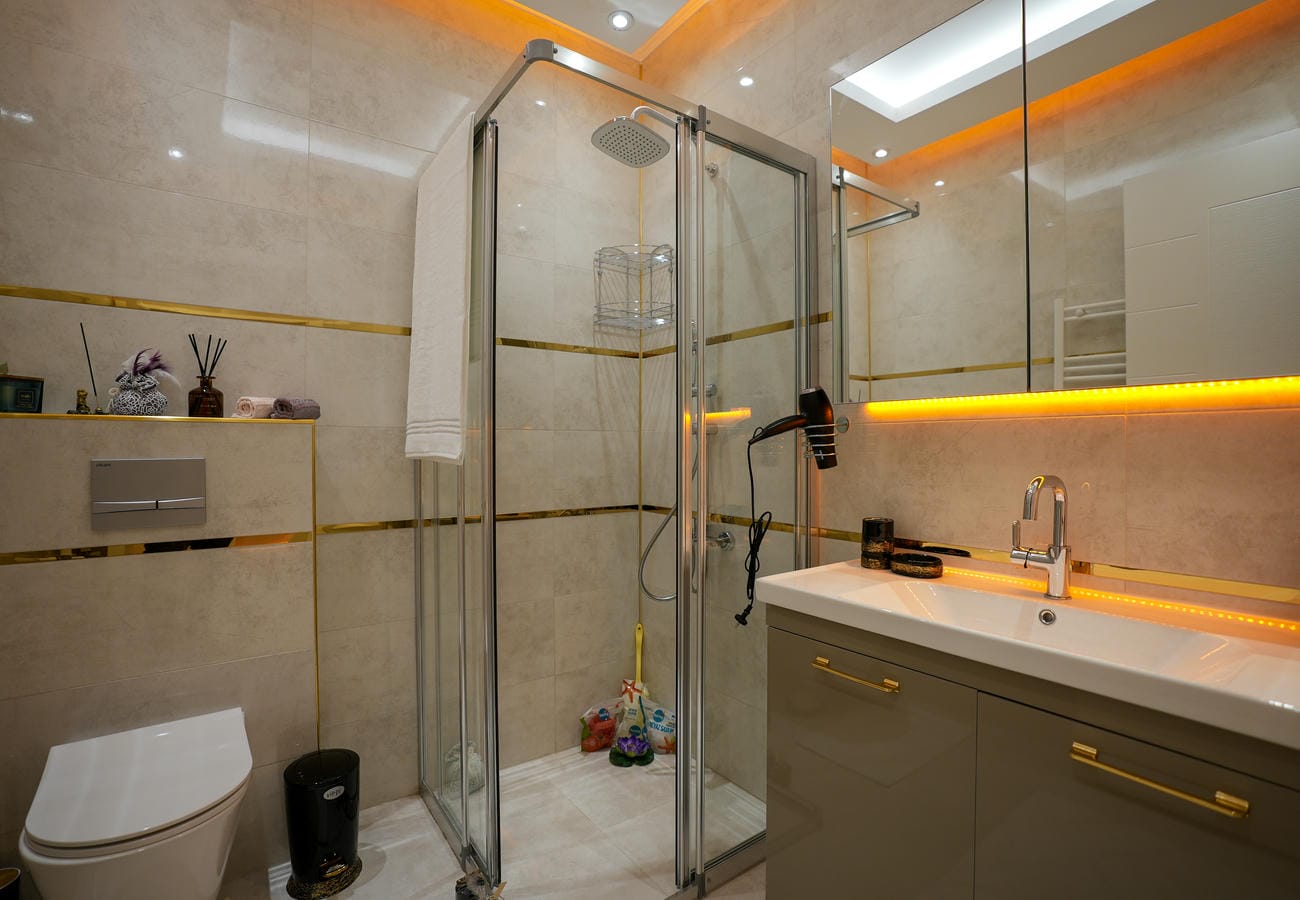 Penthouse banyosunda kare tepe duşu, asma klozet ve turuncu aydınlatmalı ayna