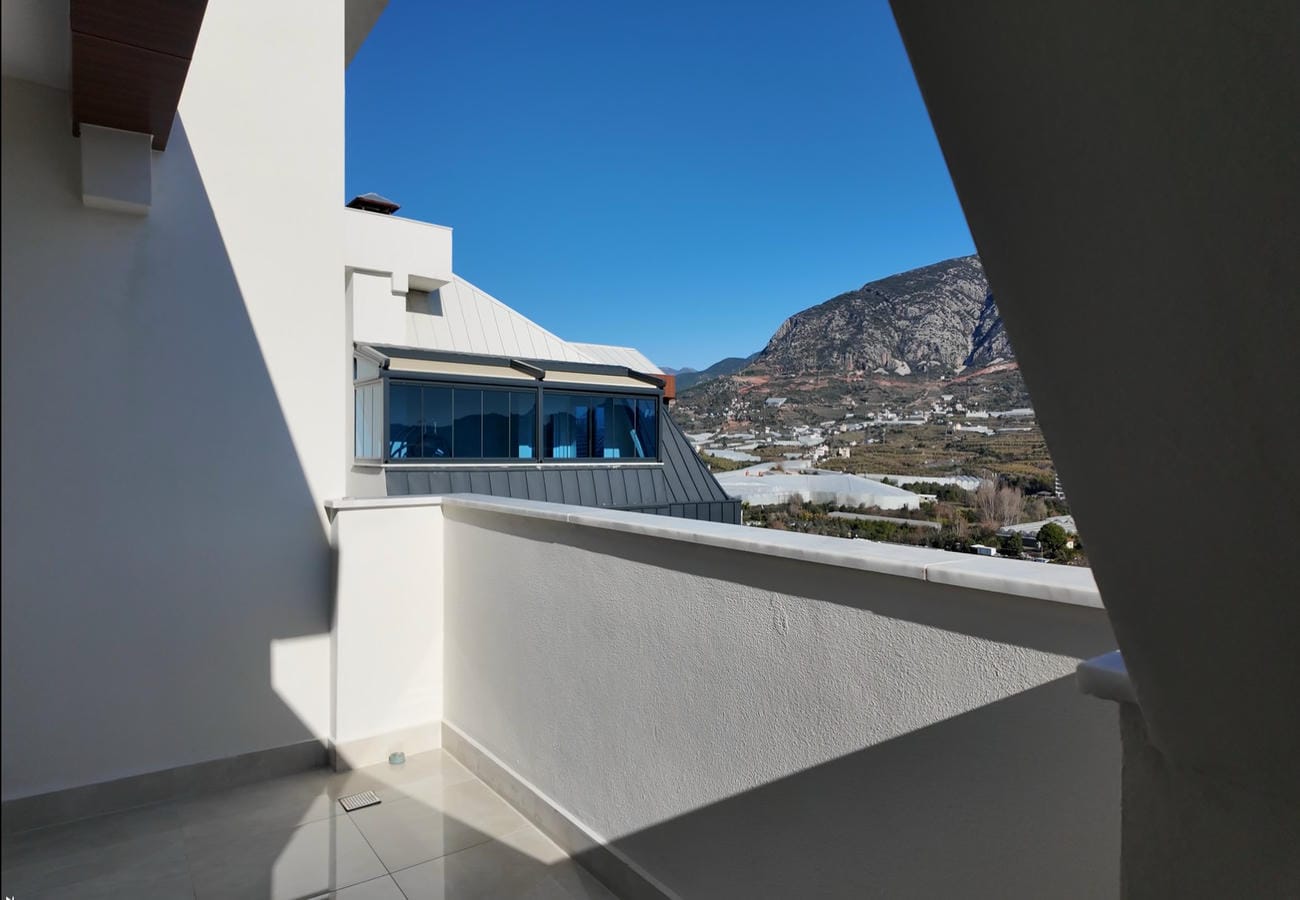 Türkiye'de satılık penthouse balkonunda beyaz parapet, dağ yamacı ve seralı vadi manzarası