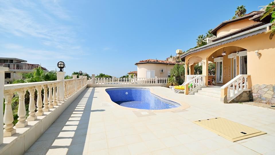 Courtyard pool beside a villa with an arched veranda, white balustrades and palms