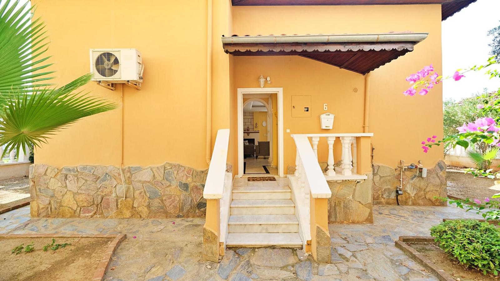 Yellow house facade with entry steps, stone base and bougainvillea in Mahmutlar, Turkey