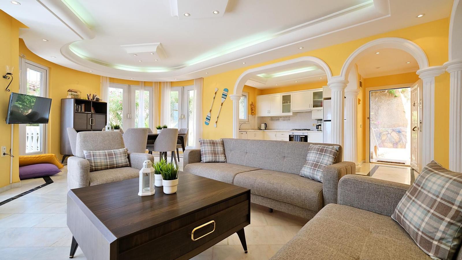 Kitchen-living room in a villa with gray corner sofas, arched openings and yellow walls