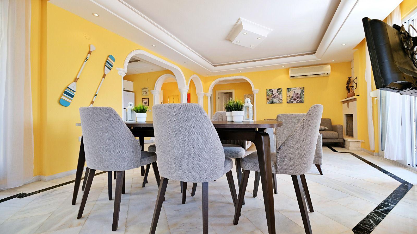 Six gray chairs around a table in the kitchen-living room of a 2+1 villa in Mahmutlar, Turkey