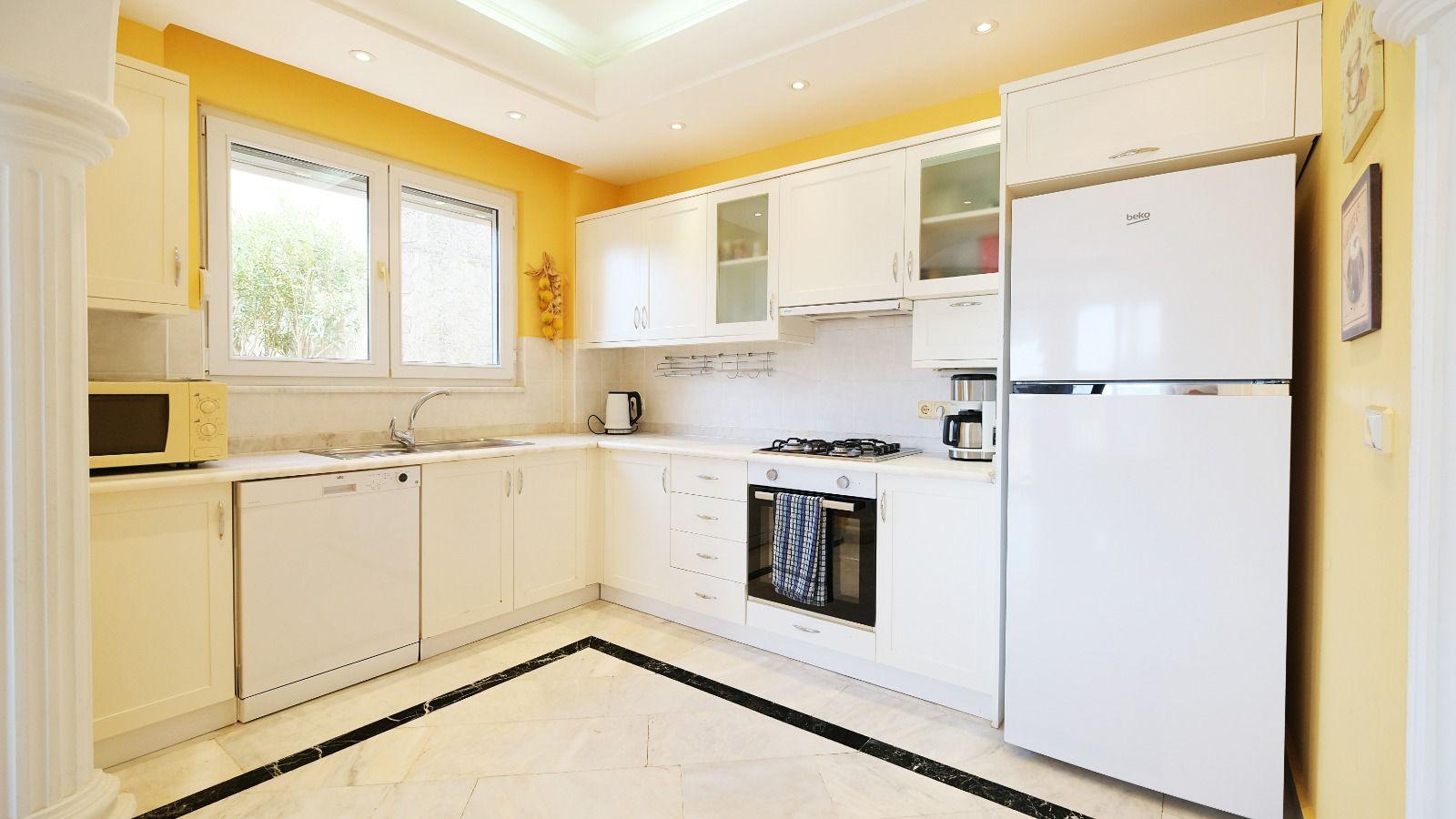 Corner white kitchen with fridge, gas hob and dishwasher in a detached home