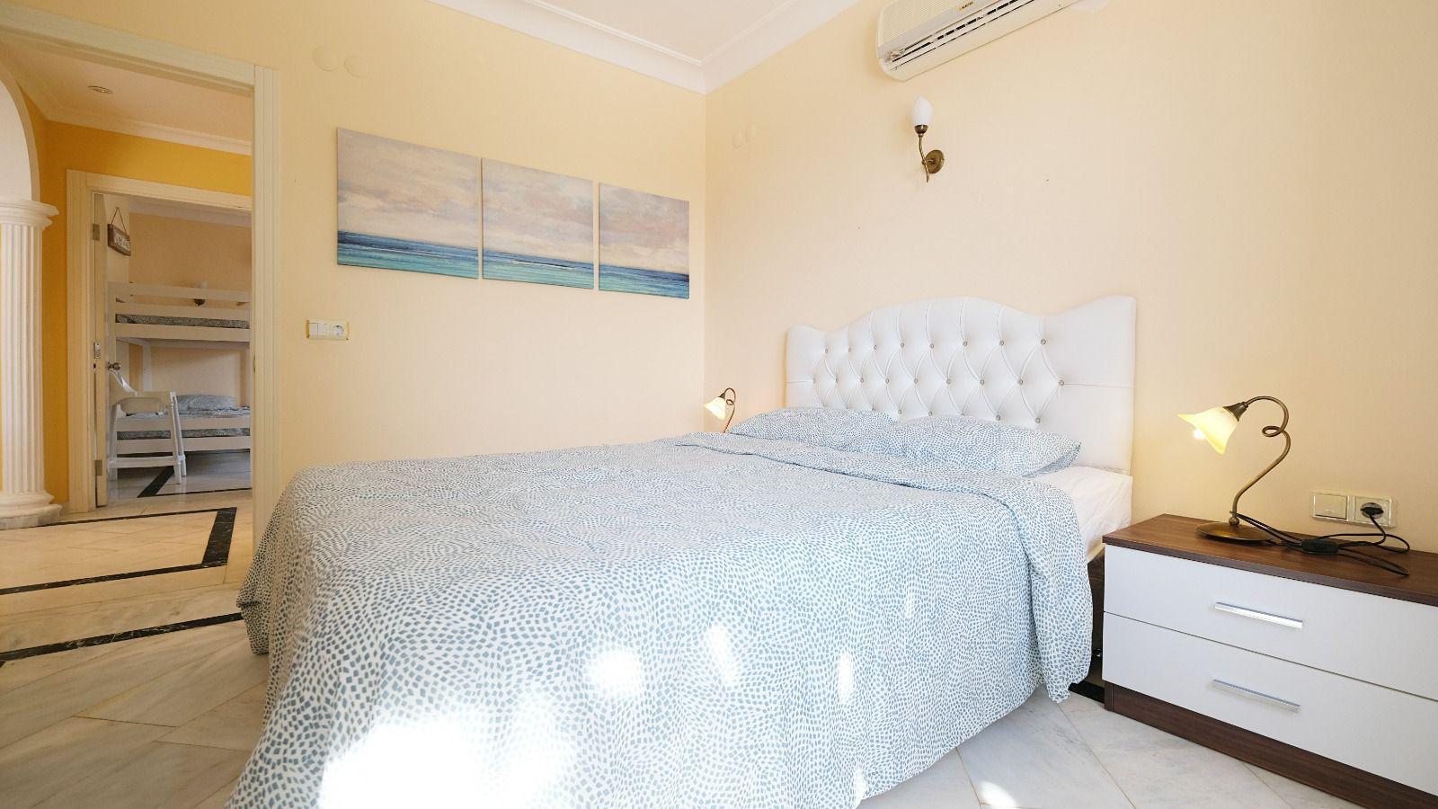 Bedroom in a villa with a double bed, white quilted headboard and wall lights