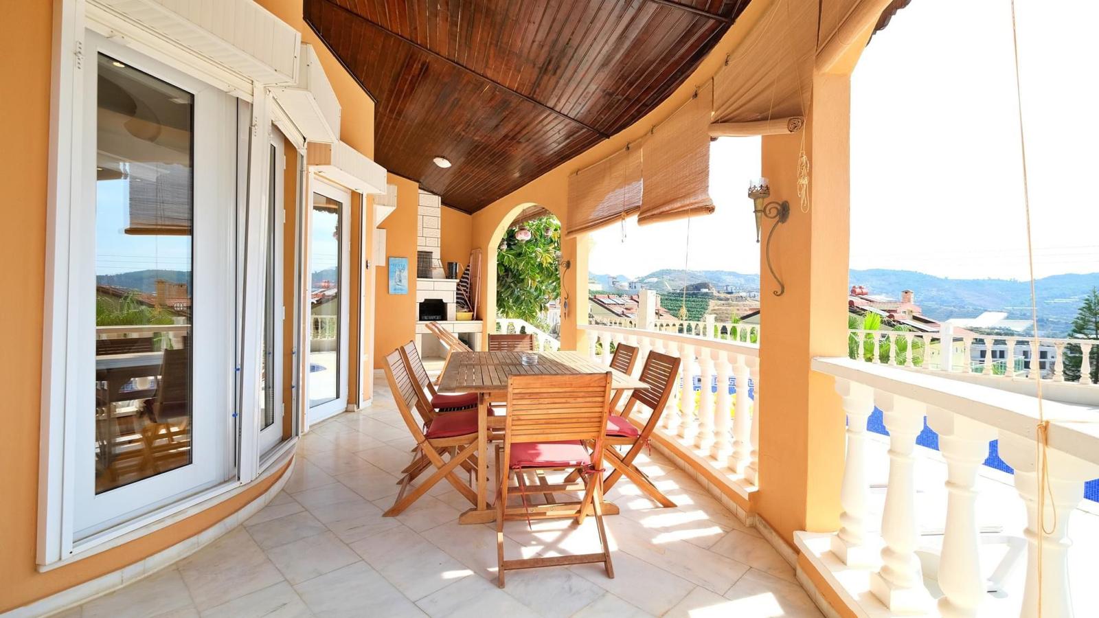 Covered terrace with wooden table, folding chairs and panoramic mountain-and-city views